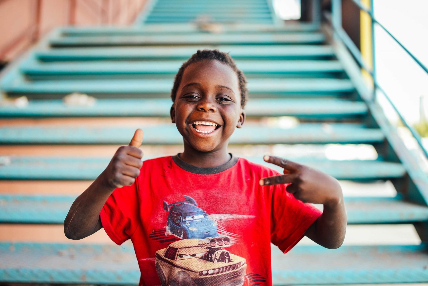 A smiling child giving a thumbs up on a stairway